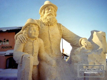 Die Skulptur zeigt einen sitzenden Wanderer mit seinem Sohn im Arm. Er hält sich an einem Felsen an.